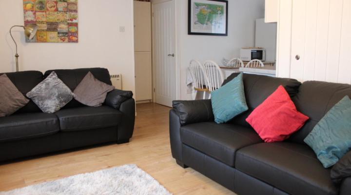 a living room with two black couches with colorful pillows at 2 bedroom Chalet all to yourself, free parking, dogs welcome in Swansea