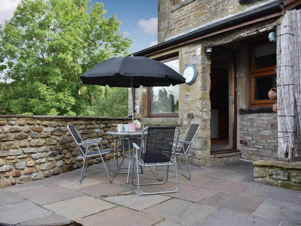 una mesa y sillas con una sombrilla en el patio en Bridge End, en Long Preston