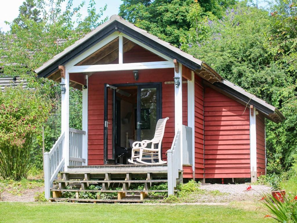 um chalé vermelho com uma cadeira no alpendre em Red Lodge - Uk10988 em Llandogo