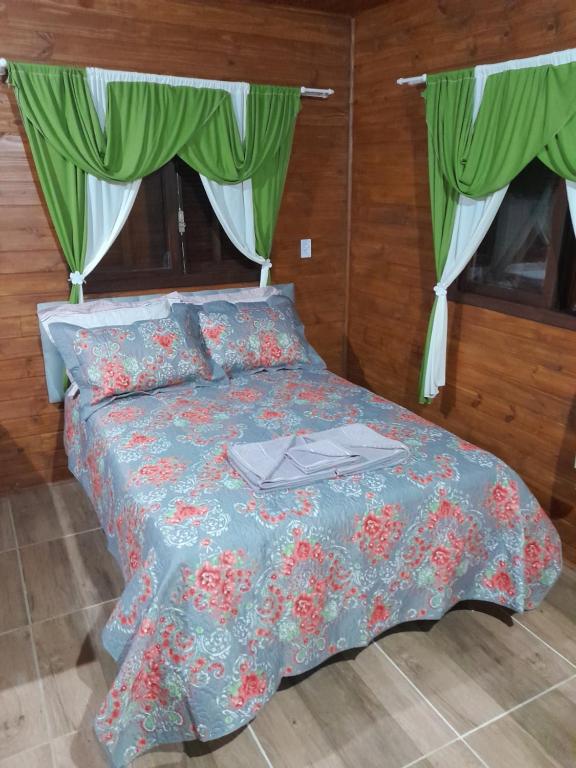 a bed with a blue comforter and green curtains at Cabanas dos Pinheiros in São Francisco de Paula
