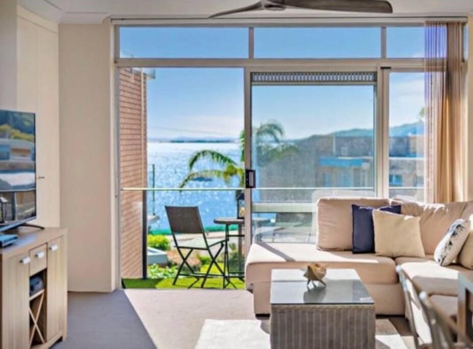 a living room with a couch and a large window at Sparkling water views over Shoal Bay beach in Shoal Bay