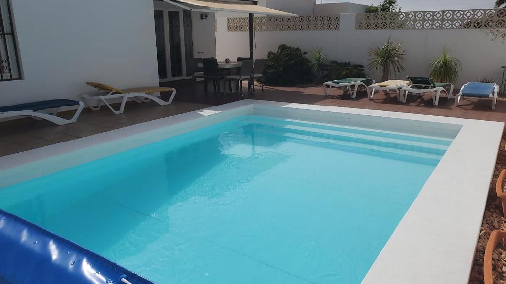 una gran piscina azul con mesas y sillas en Villa Acoran, en Costa Teguise