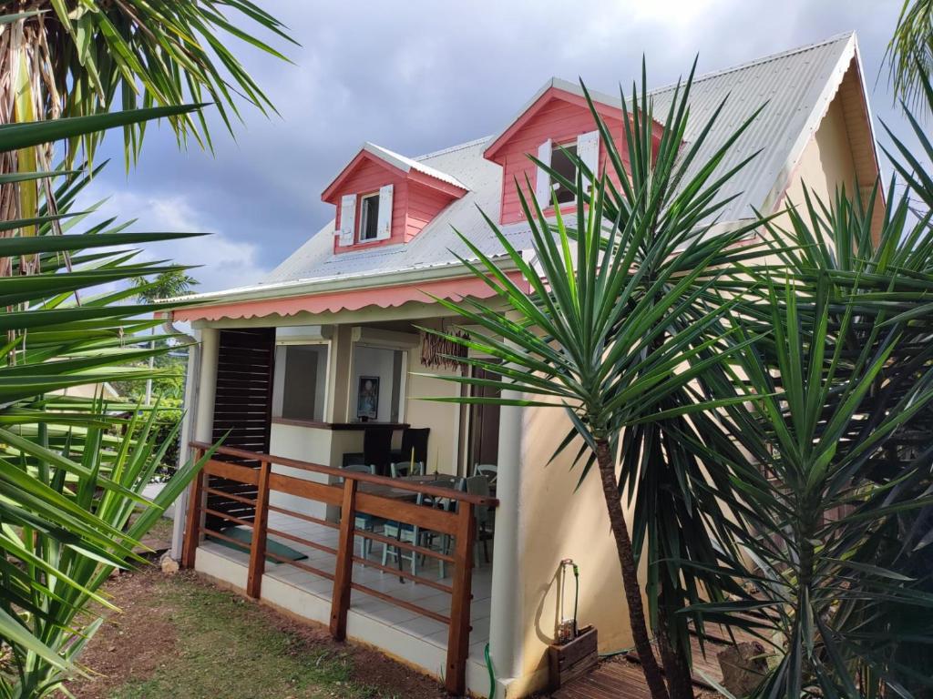 uma casa com um telhado vermelho e algumas palmeiras em Charmante villa avec accès direct à la mer em Sainte-Rose