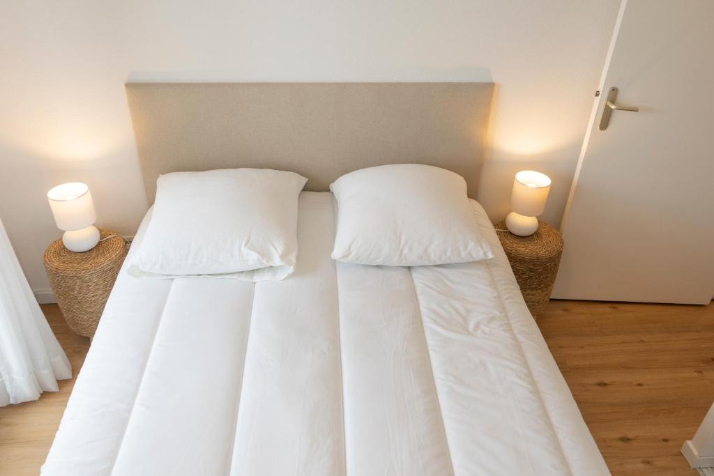 a bedroom with two beds with white sheets and two lights at 2 pièces Port Cabourg - 2 à 4 personnes - 34 m2 - Balcon - Vue Port - Nouveau sur Booking ! in Dives-sur-Mer