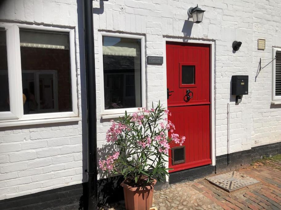 a red door and a plant in front of a building at Beautiful mews cottage. Ledbury town centre. in Ledbury