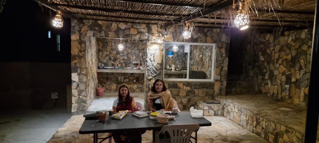 Dwie kobiety siedzące przy stole w kamiennym pokoju w obiekcie Balcony walk rest house Jabal shams w mieście Sa‘ab Banī Khamīs