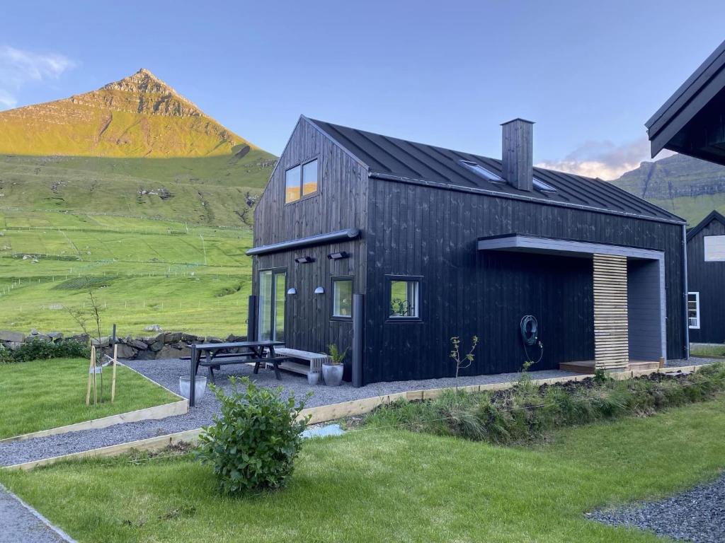 uma casa negra com um banco à frente. em Okkara summarhús við Gjógv - Luxury cottage - Unique location em Við Gjógv