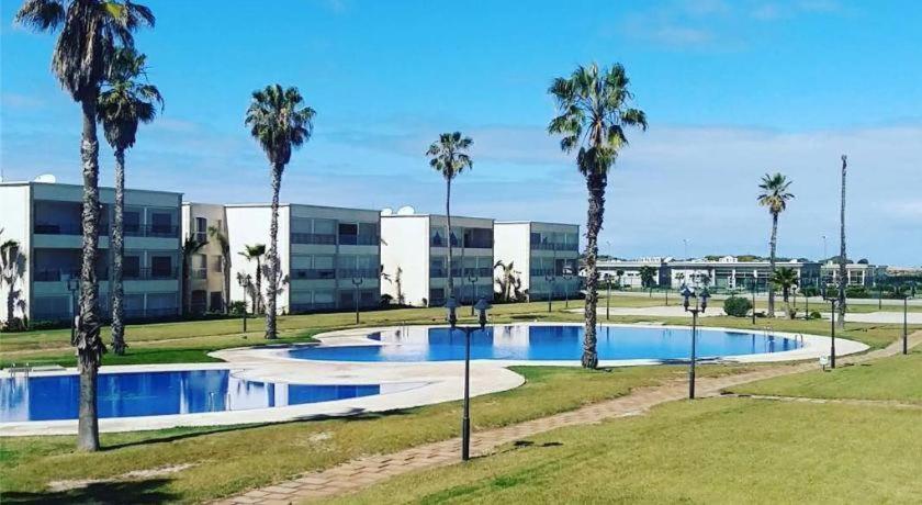 a large pool with palm trees in front of a building at Ola Blanca Sidi rahal Apparthotel in Sidi Rahal