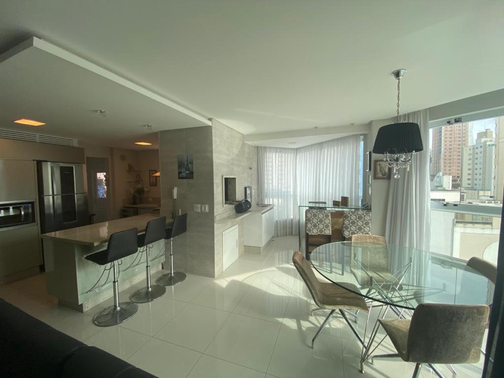 cocina y sala de estar con mesa de cristal y sillas en Espaçoso e aconchegante, en Balneário Camboriú