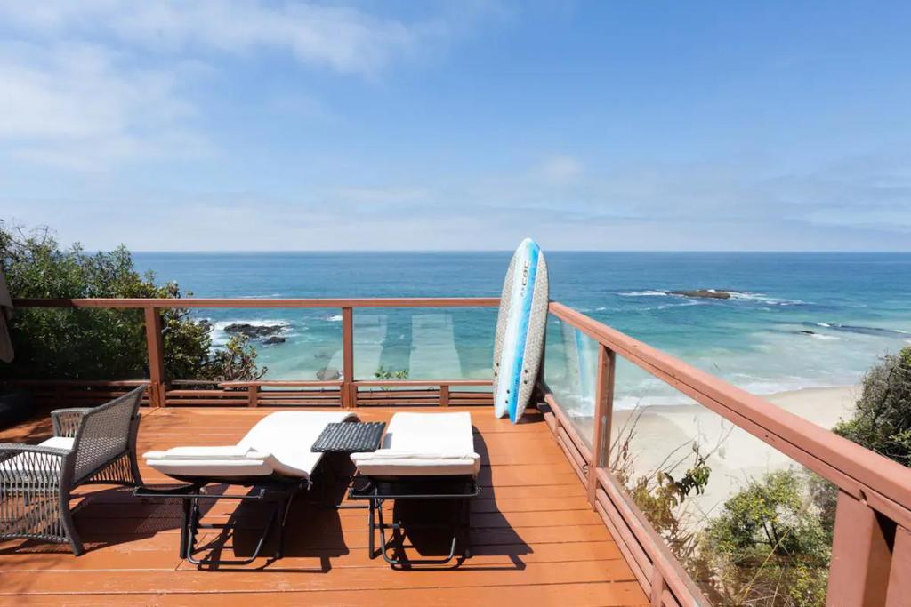 a table and chairs on a balcony with a surfboard at OCEAN FRONT Beach HOUSE! Private Stairs to SAND! in Laguna Beach