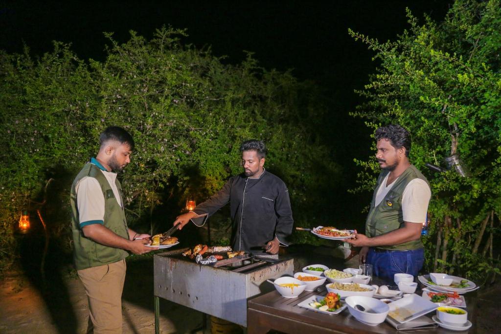 three men standing around a grill with plates of food at Leopard Nest - Glamping in Yala in Yala