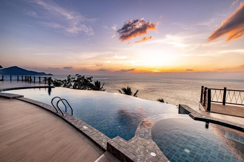 a swimming pool next to the ocean at sunset at The AVA Resort Koh Tao in Koh Tao