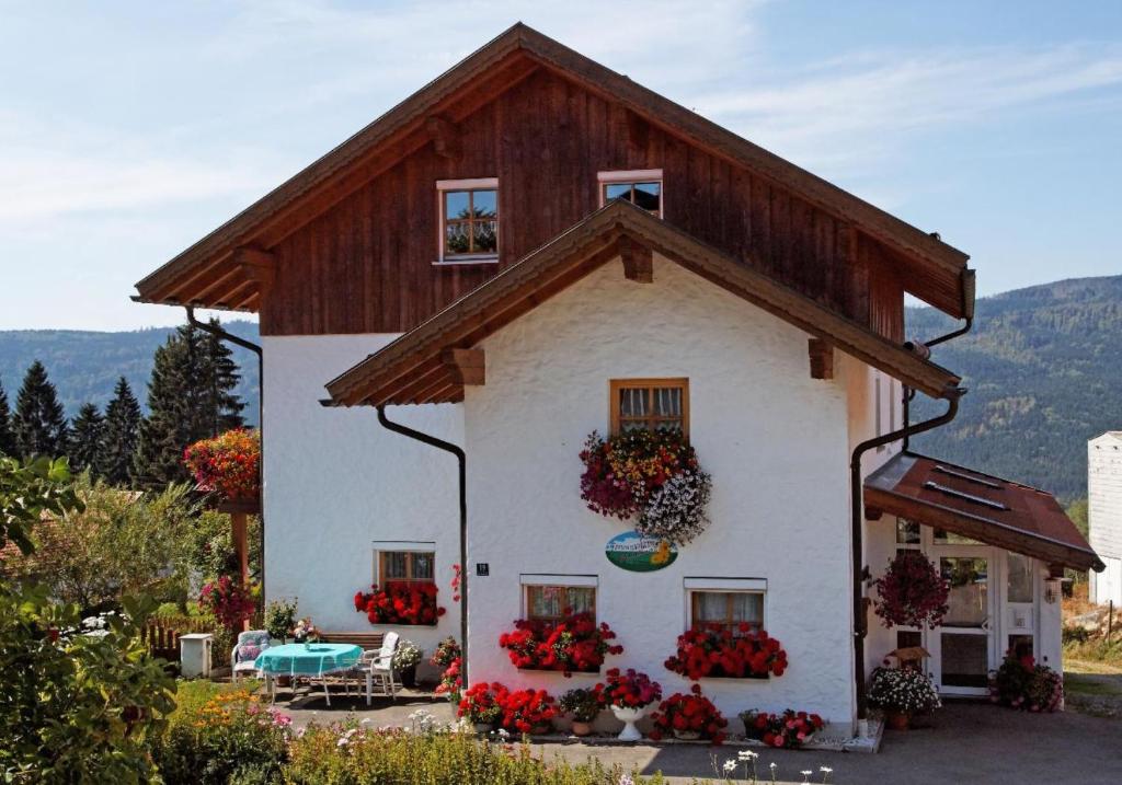 a white house with a wooden roof and flowers at Ferienwohnung Christina in Mauth