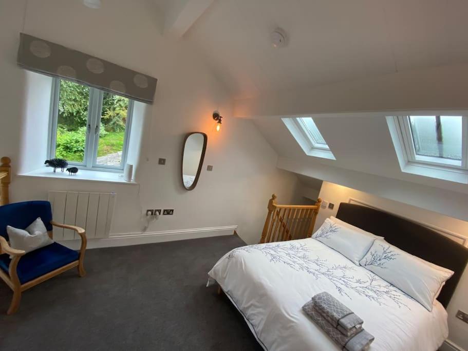 a bedroom with a bed and a chair and windows at Brigstone Stable - charming peaceful cottage in Lothersdale