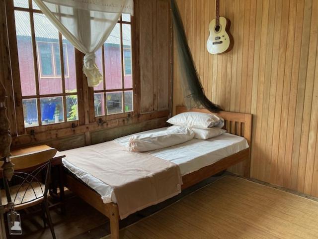 Bett in einem Zimmer mit Fenster und Gitarre in der Unterkunft Areef Homestay Kaledupa in Kaledupa
