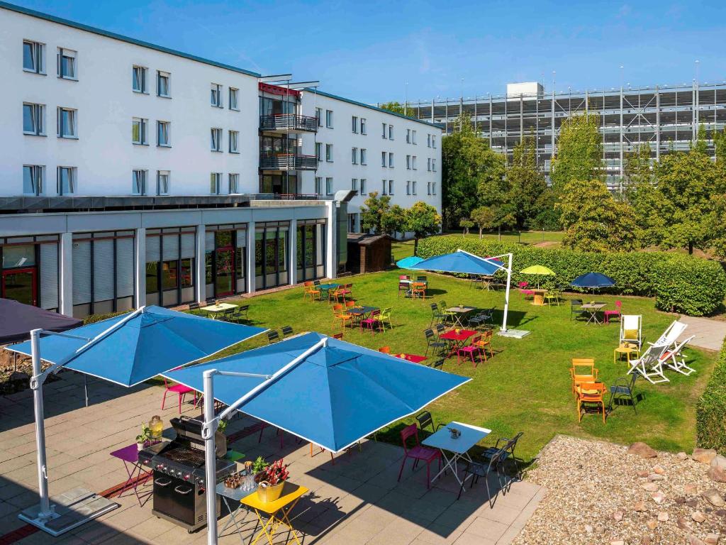 Greet hotel Darmstadt - an Accor hotel - في دارمشتات: فناء خارجي به طاولات وكراسي ومظلات زرقاء