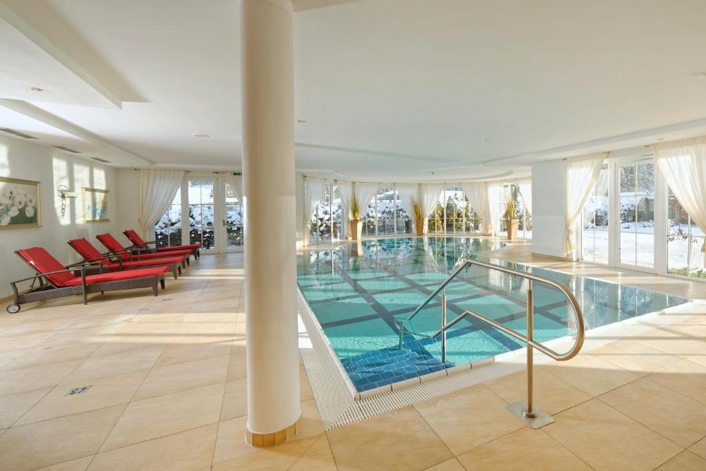 a large swimming pool in a building with red chairs at Ortnerhof -Das Wohlfühlhotel in Ruhpolding