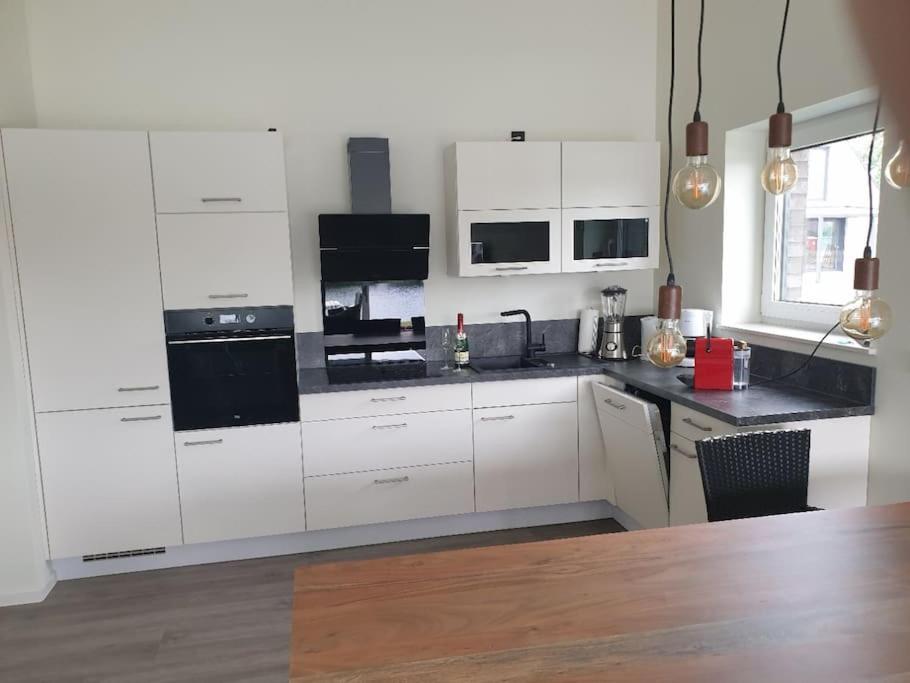 eine Küche mit weißen Schränken und schwarzen Geräten in der Unterkunft Ferienhaus mit privatem Seezugang, Sauna, Strand, Wassersport, Ruderboot, Stand Upp in Barßel