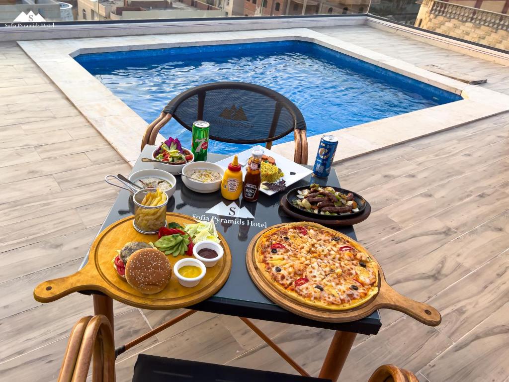 Sofia Pyramids Hotel في القاهرة: طاولة عليها بيتزا وطعام بجانب مسبح