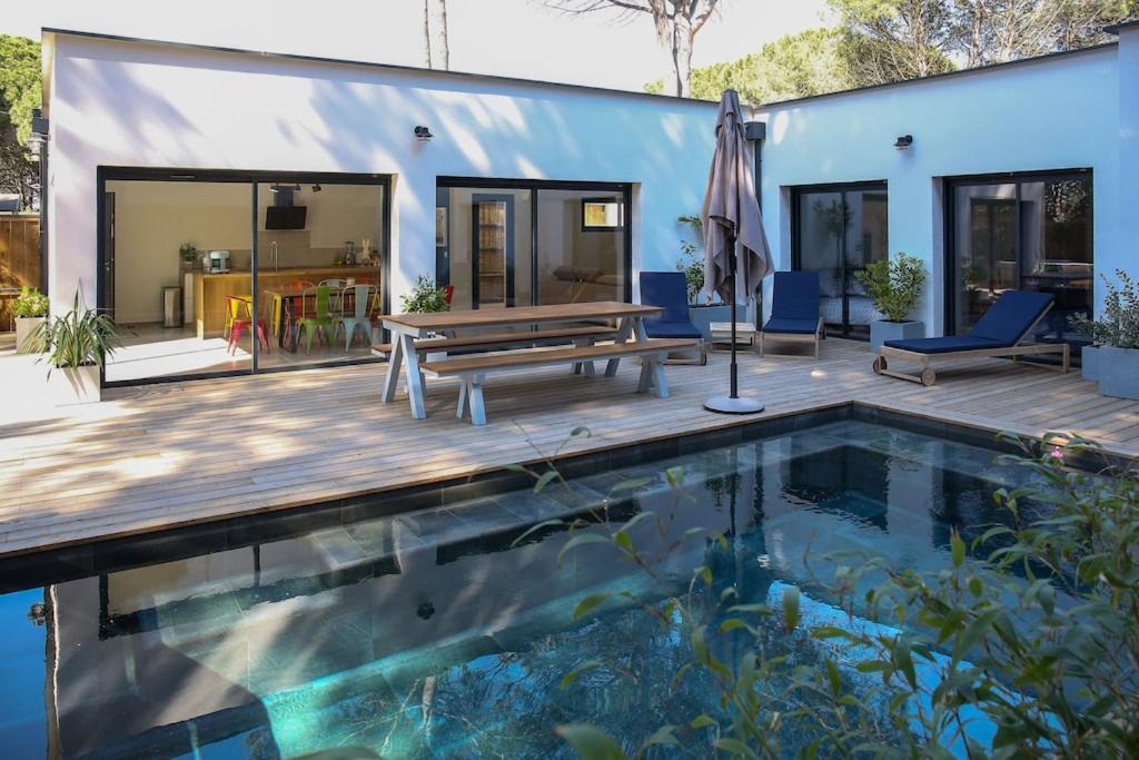 a house with a pool and a wooden deck with a picnic table at Contemporary house with heated pool in a magnificent pine forest in Aigues-Mortes