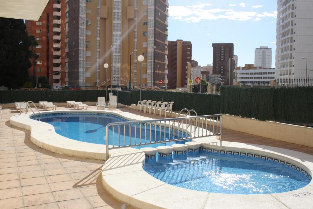 een groot zwembad met stoelen eromheen in een stad bij Apartamentos Benimar - SABESA in Benidorm