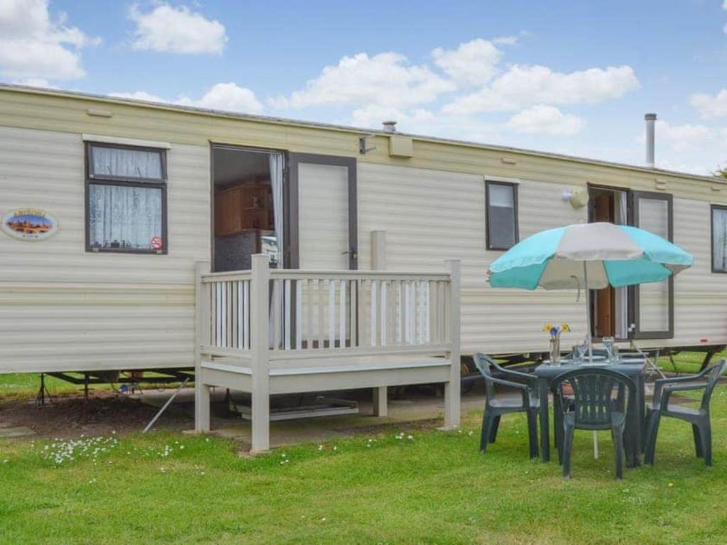 a table and chairs with an umbrella in front of a caravan at Norfolk Poppy Caravan - Sleeps 4 - WiFi and Sky TV Included in Bacton