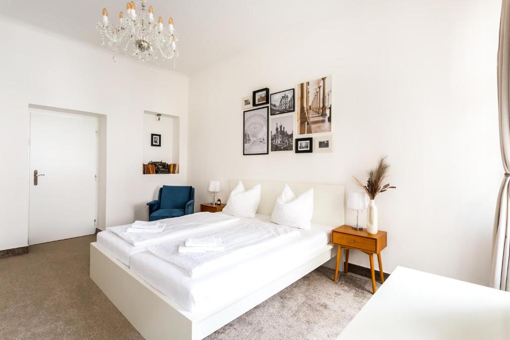 a white bedroom with a white bed and a blue chair at Apartmá Zeyer 1887 in Karlovy Vary