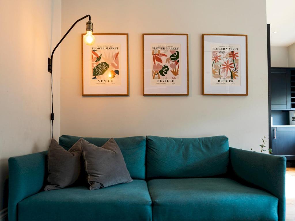 um sofá azul numa sala de estar com quatro fotografias na parede em Pass the Keys Stylish cosy 2bed near Finsbury Park w balcony em Londres