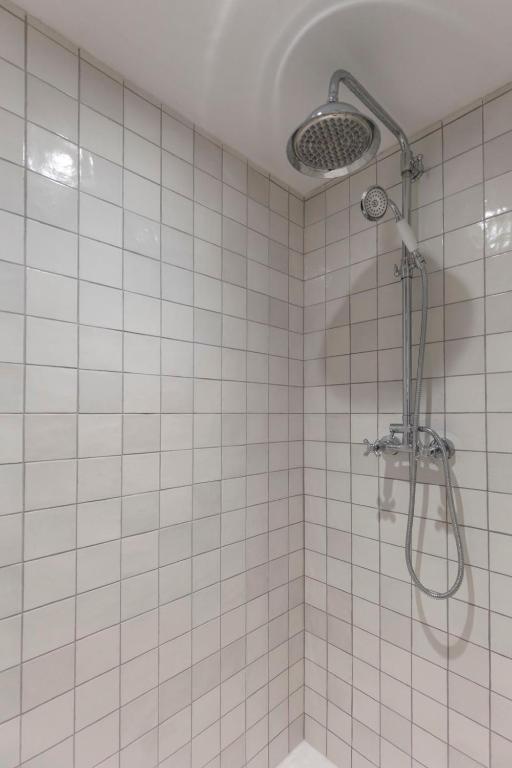 a white tiled bathroom with a shower with a shower head at La Demeure du Clocher 4 - On the Port and Place St Catherine - 8 P in Honfleur