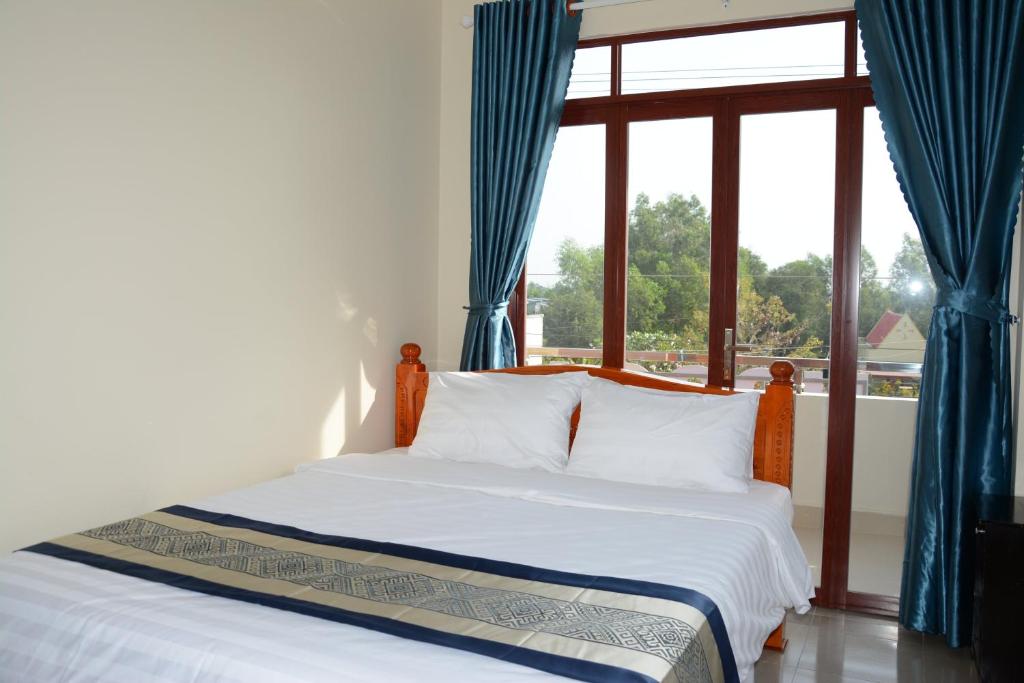 a bedroom with a bed and a window with blue curtains at NGOC LINH MOTEL in áº¤p VÄ©nh ÃÃ´ng