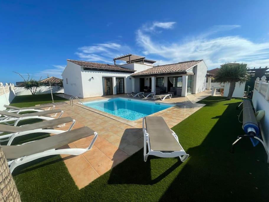a swimming pool with lounge chairs and a house at Stunning Villa Amanecer in Corralejo