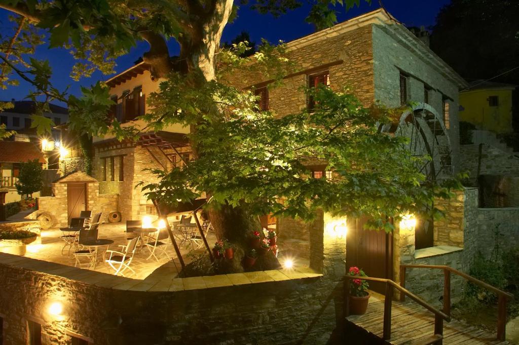 un edificio con un árbol delante de él por la noche en Palio Eleotrivio Guesthouse, en Agios Lavredios