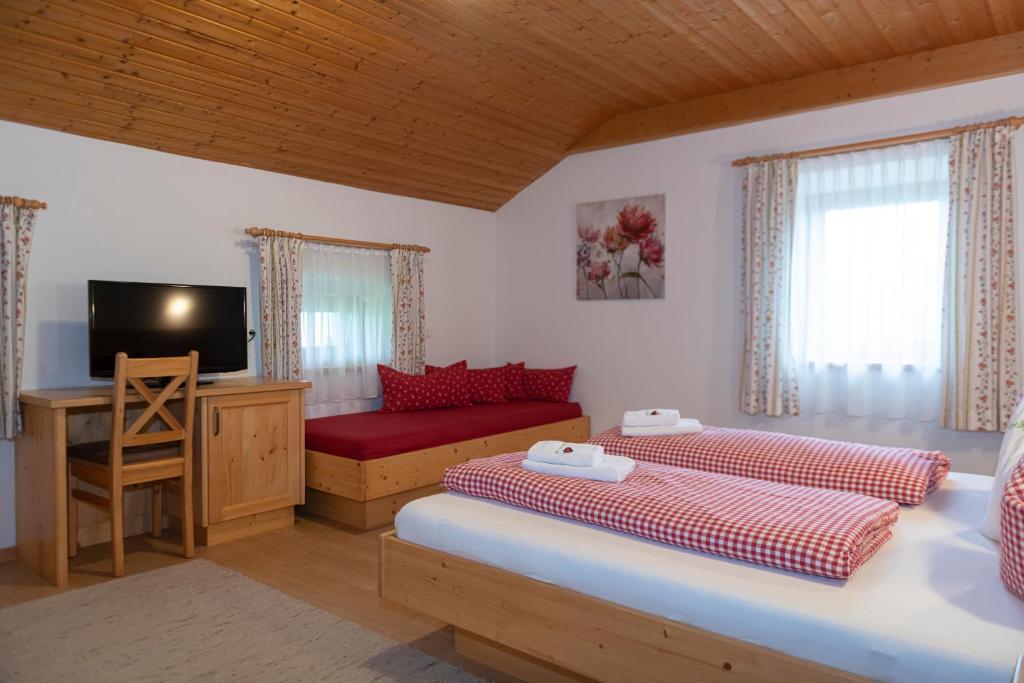 a bedroom with two beds and a desk and a television at Hartlhof Urlaub am Baby- und Kinderbauernhof in Niederau