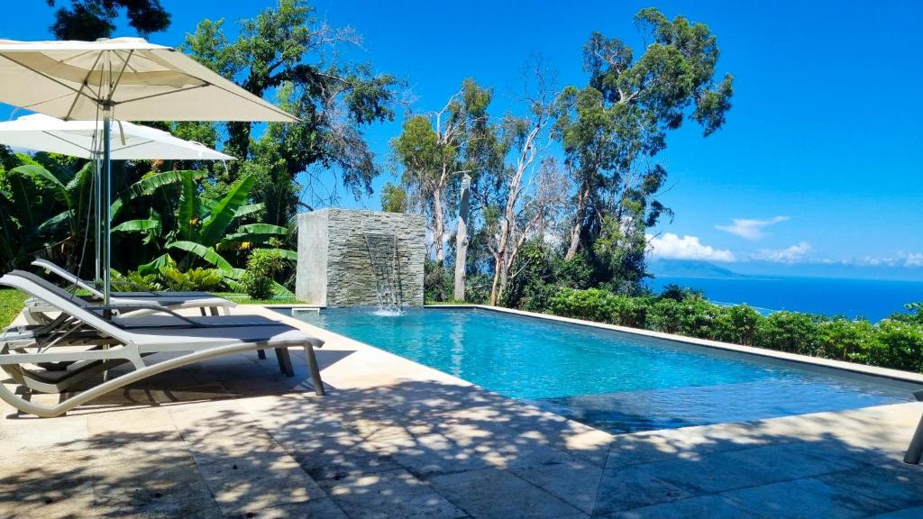 a swimming pool with two chairs and an umbrella at Horizon Hill Villa in Pirae