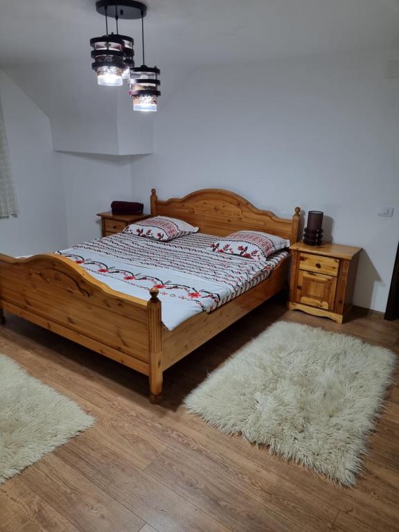 1 dormitorio con cama de madera, mesita de noche y 2 alfombras en Cabana Trei Brazi Bucovina cu ciubar en Gura Humorului