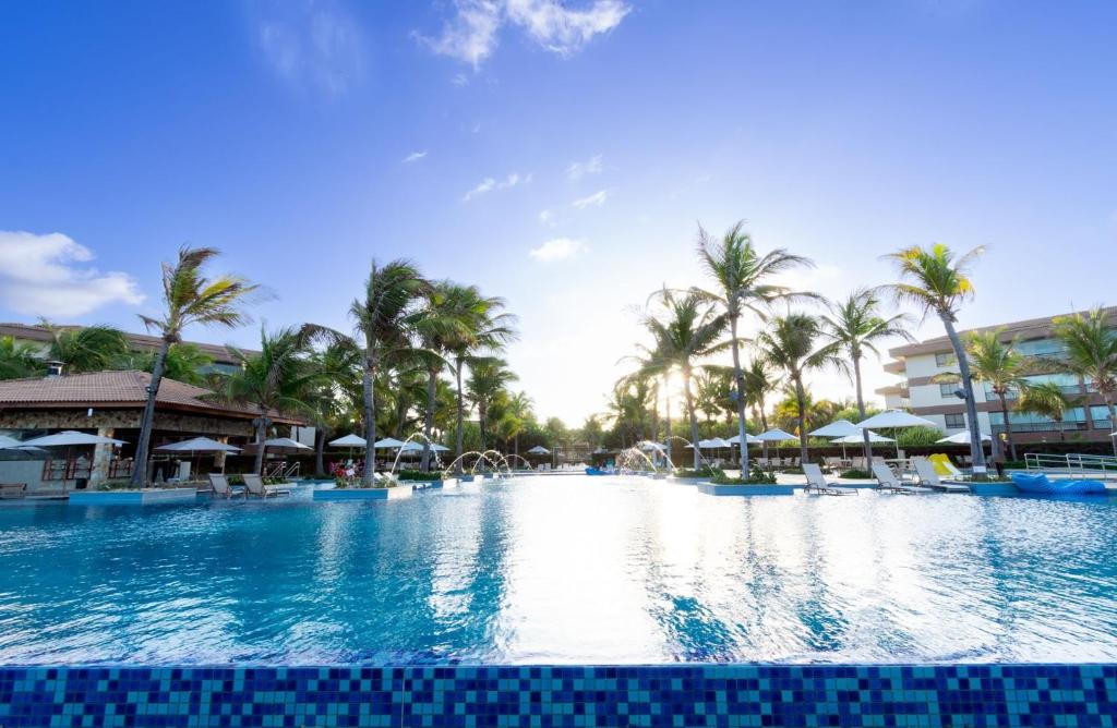 a pool at a resort with palm trees and umbrellas at Mandara Lanai Apartamento Bangalô in Aquiraz