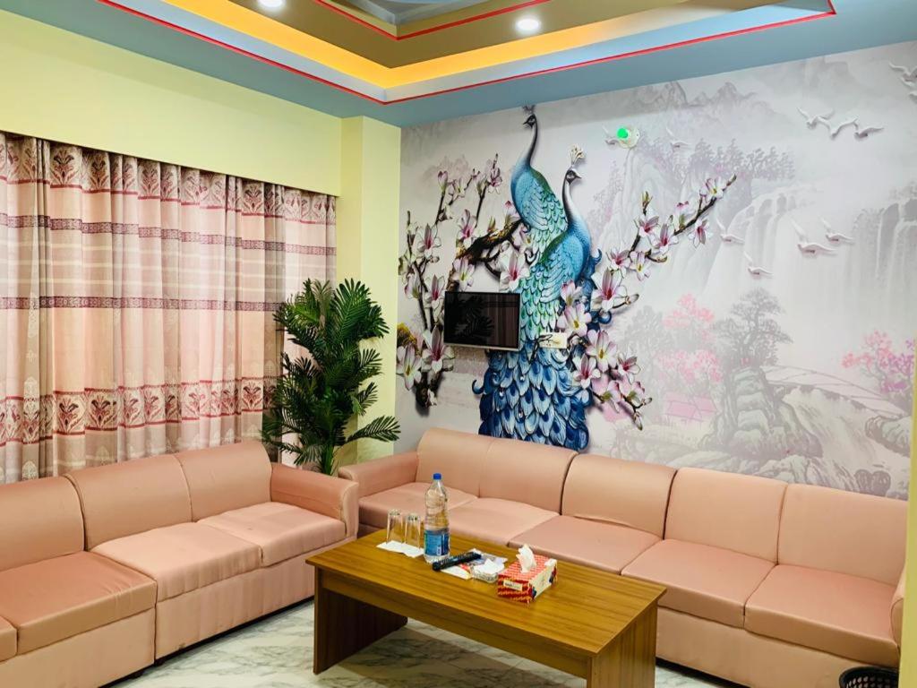 Hotel Pushpo Bilash في Khulna: غرفة معيشة مع أريكة وجدارية طاووس