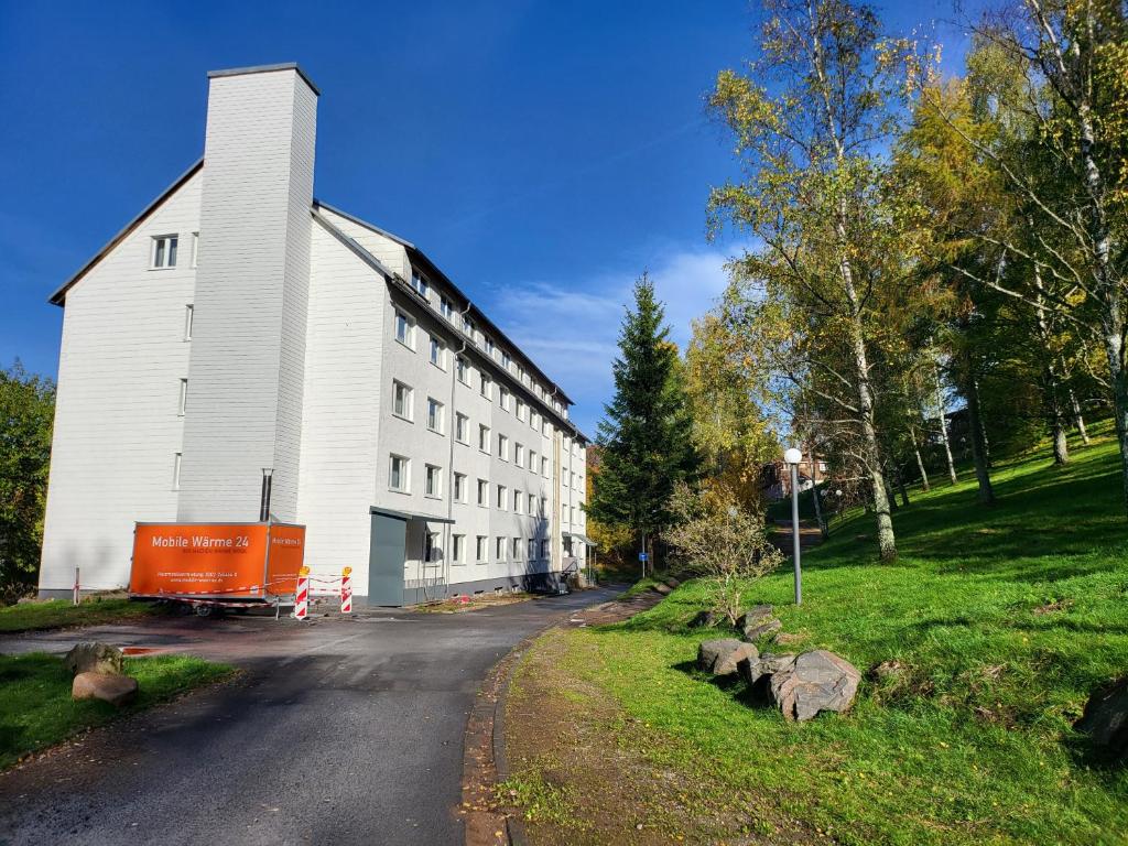 Eine weiße Scheune mit einem orangenen Truck, der neben einer Straße parkt. in der Unterkunft Werrapark Resort Hotel Am Sommerberg in Masserberg