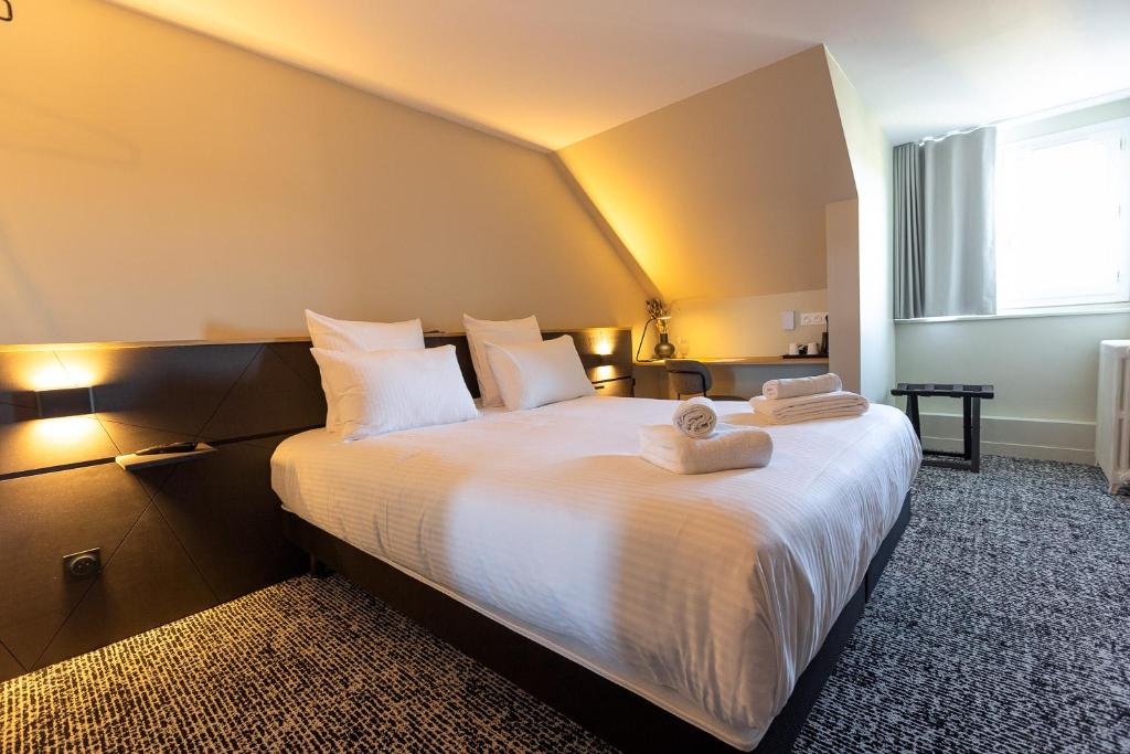 una camera da letto con un grande letto bianco con asciugamani di Logis Hôtel & Restaurant Le Vert Bocage a Franqueville-Saint-Pierre