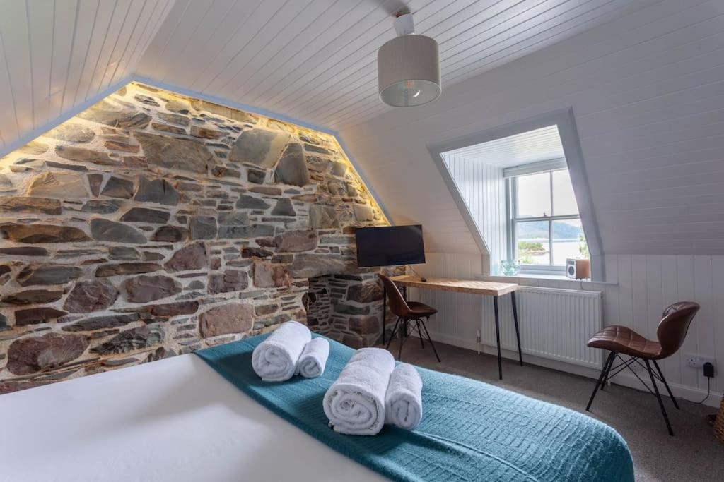 a bedroom with a stone wall and a bed with towels at Plockton Sea View Apartment in Plockton