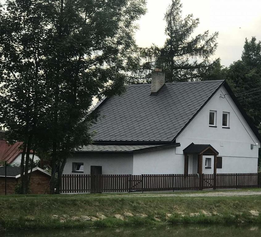 a white house with a black roof and a fence at Chalupa ve Sněžném in Sněžné