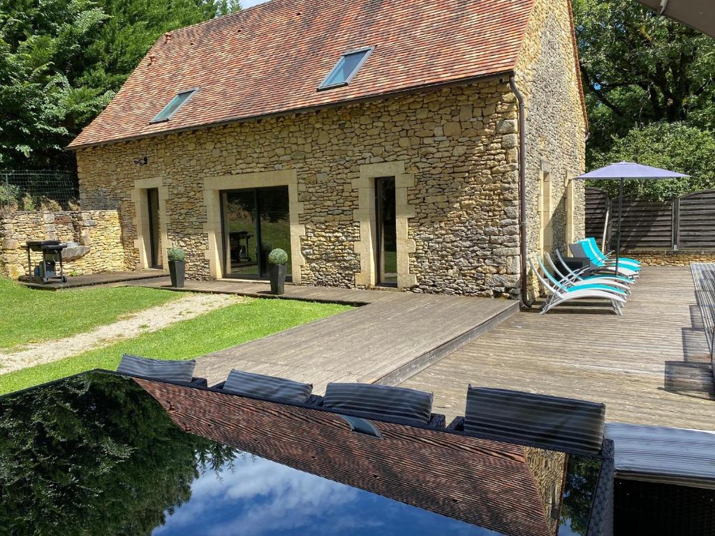 a house with a wooden deck with chairs next to the water at La Truffière du Vignou in Archignac