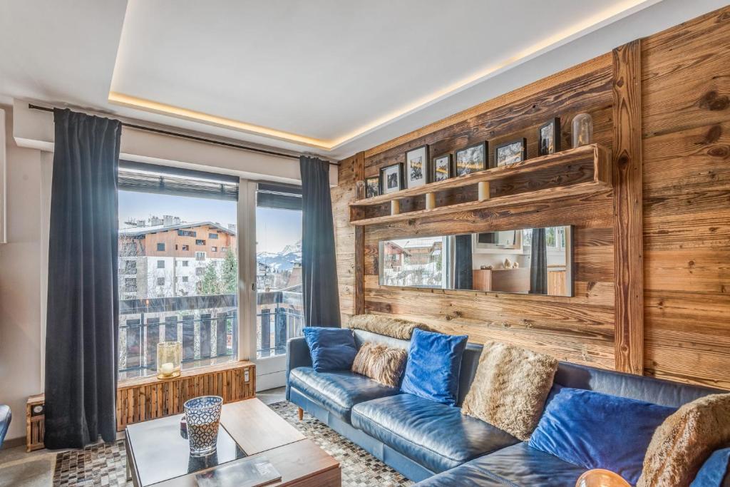 a living room with a blue couch and a large window at Superb ski-in apartment in Megève - Welkeys in Megève