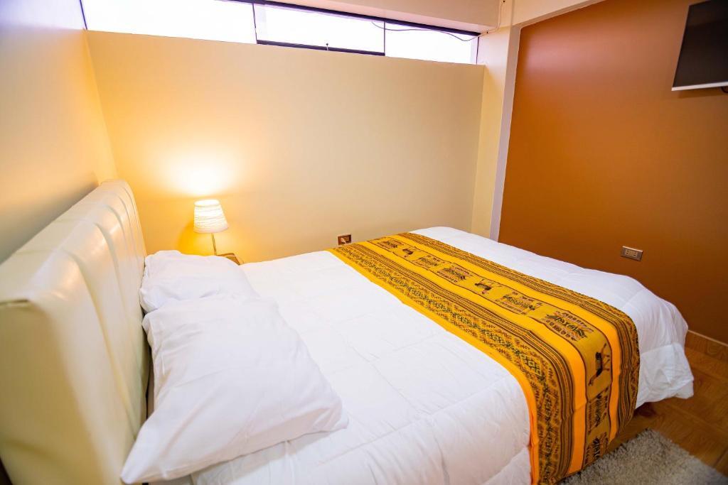a bedroom with a white bed with a yellow blanket on it at Departamento KIRI para familias con terraza cerca al Aeropuerto de Juliaca in Juliaca