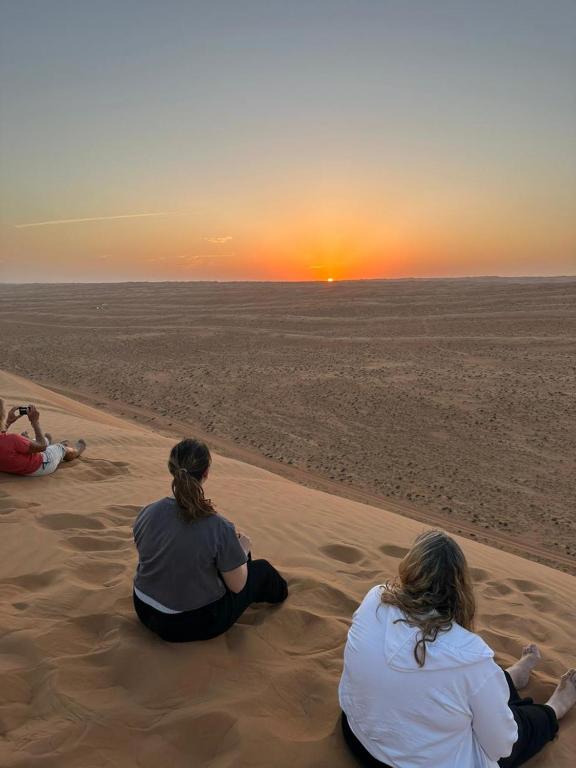 three people sitting in the sand watching the sunset at Moon Light Camp in Bidiyah
