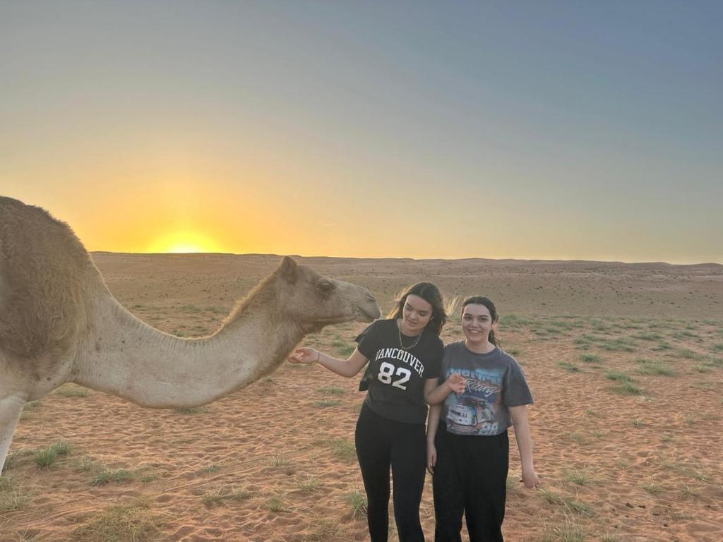 two women standing next to a camel in the desert at Moon Light Camp in Bidiyah