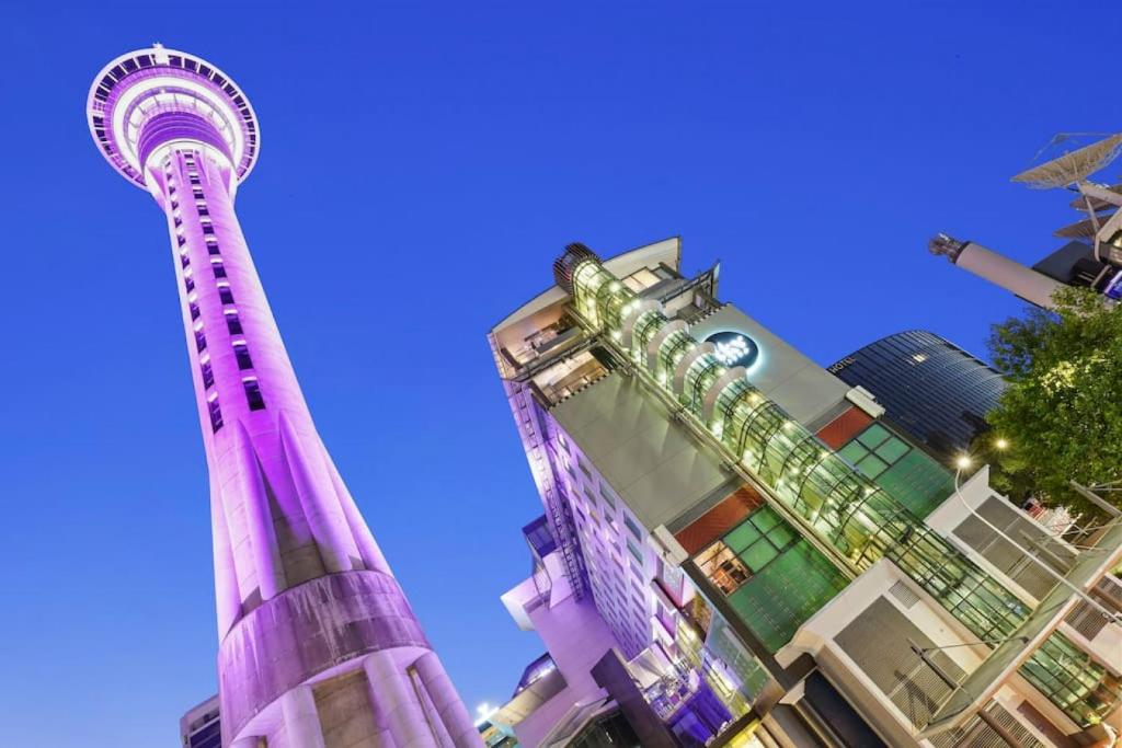 a tall purple tower in front of some buildings at CBD Stunner - Skytower View - WIFI - Netflix in Auckland