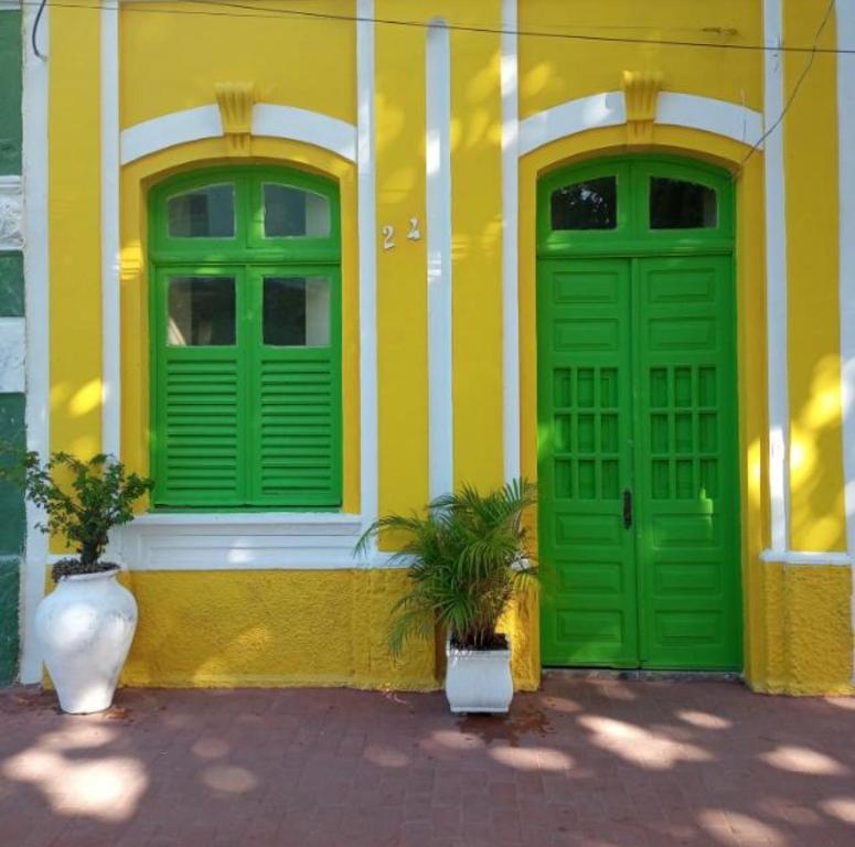 un bâtiment jaune avec des portes vertes et deux plantes en pot dans l'établissement Casa da Lu, à Olinda