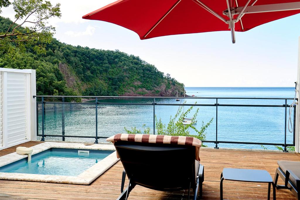 a deck with a chair and an umbrella and a pool at LES GALETS ROUGES LODGES & SPA in Bouillante
