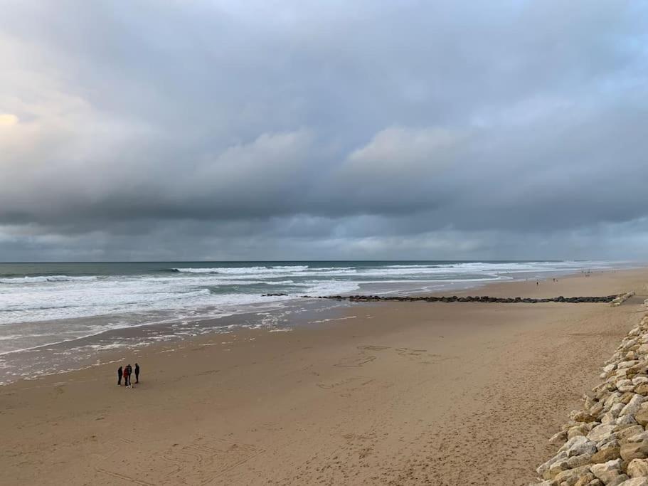 Agréable T2 Lacanau Ocean bord de mer. Expo sud. في لاكانو-أوسيان: شخصان يسيران على شاطئ قريب من المحيط